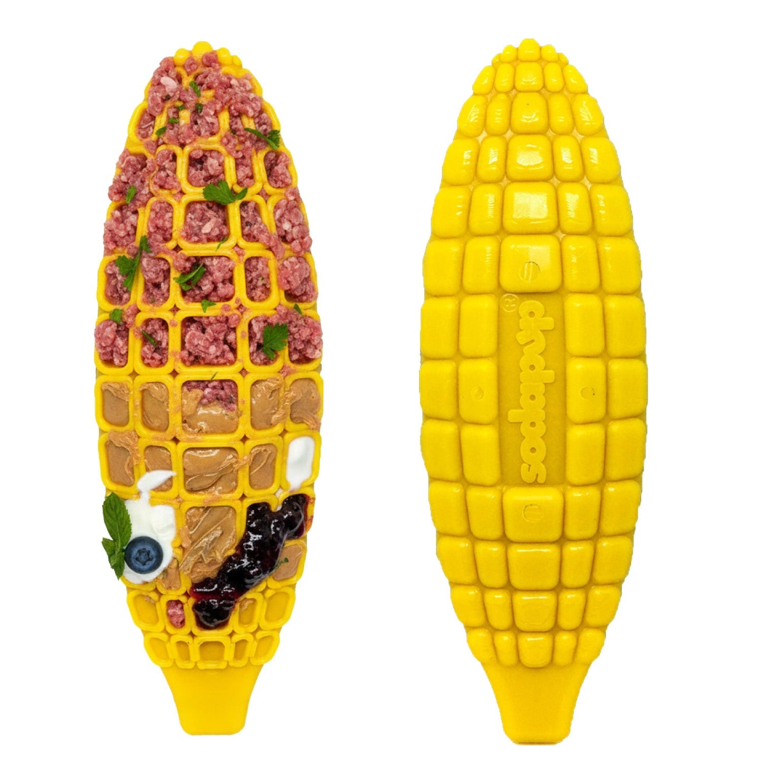 Two yellow, corn-shaped SodaPup Corn on the Cob EChew Ultra Durable Nylon Dog Chew Toys are shown—one empty, the other filled in its square sections with ground meat, herbs, nut butter (like for a dog toy), a blueberry, and dark jam.