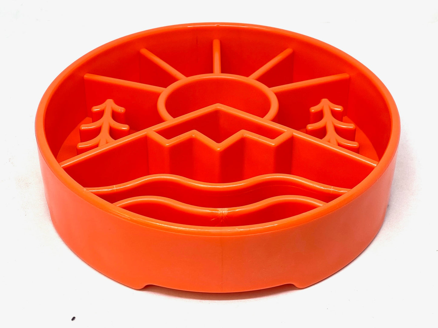 The Great Outdoors Design EBowl Enrichment Slow Feeder Bowl for Dogs by SodaPup is a round, orange feeding puzzle for pets featuring raised designs of trees, a mountain, a large sun, and wavy lines at the bottom. This slow feeder bowl's raised sections create various compartments for pet food, promoting healthy slower eating.