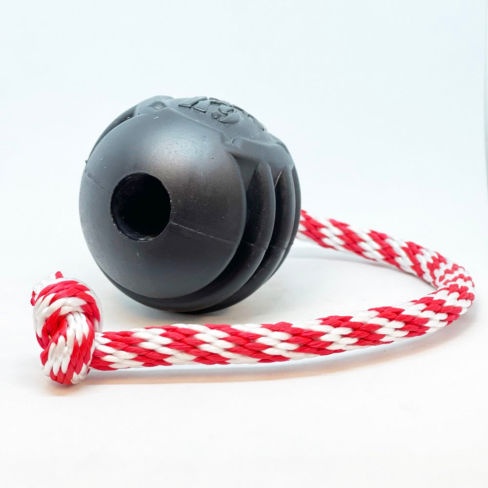 The SodaPup USA-K9 Magnum Black Stars and Stripes Ultra-Durable Rubber Chew Toy features a black rubber ball on a red and white braided rope, perfect for power chewers as a chew, tug, or retrieval toy. Set against a plain white background.