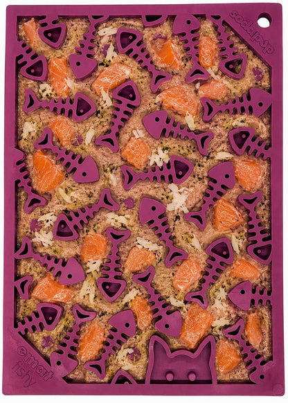 The SodaPup Fishy Design EMat Enrichment Lick Mat - Small is a purple silicone tray with fish-shaped, fish bone pattern compartments and a cat outline, ideal for serving raw salmon and herbs as pet treats.