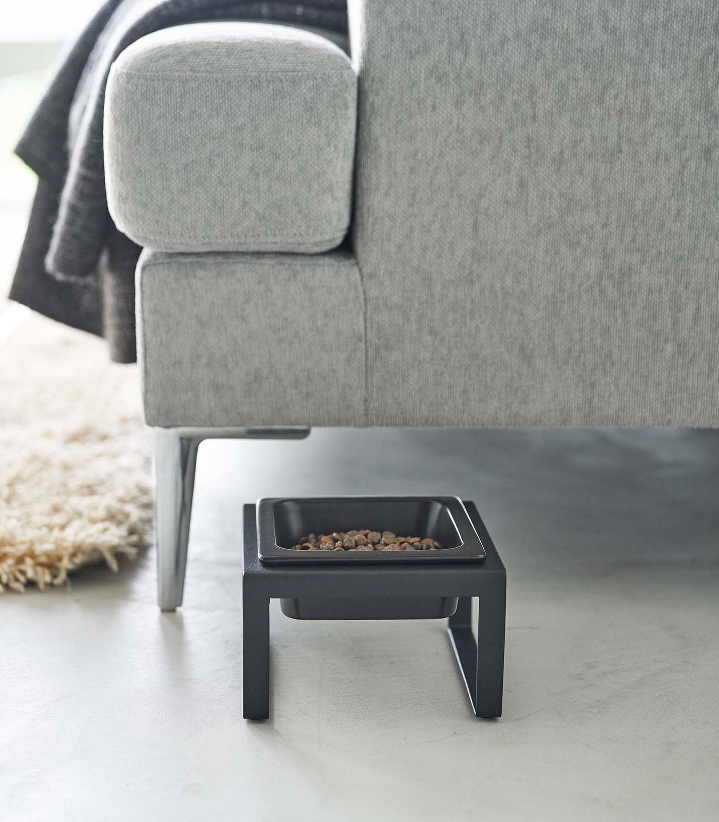 A Single Pet Food Bowl - Two Styles - Steel + Ceramic by Yamazaki Home on the floor next to a gray couch.