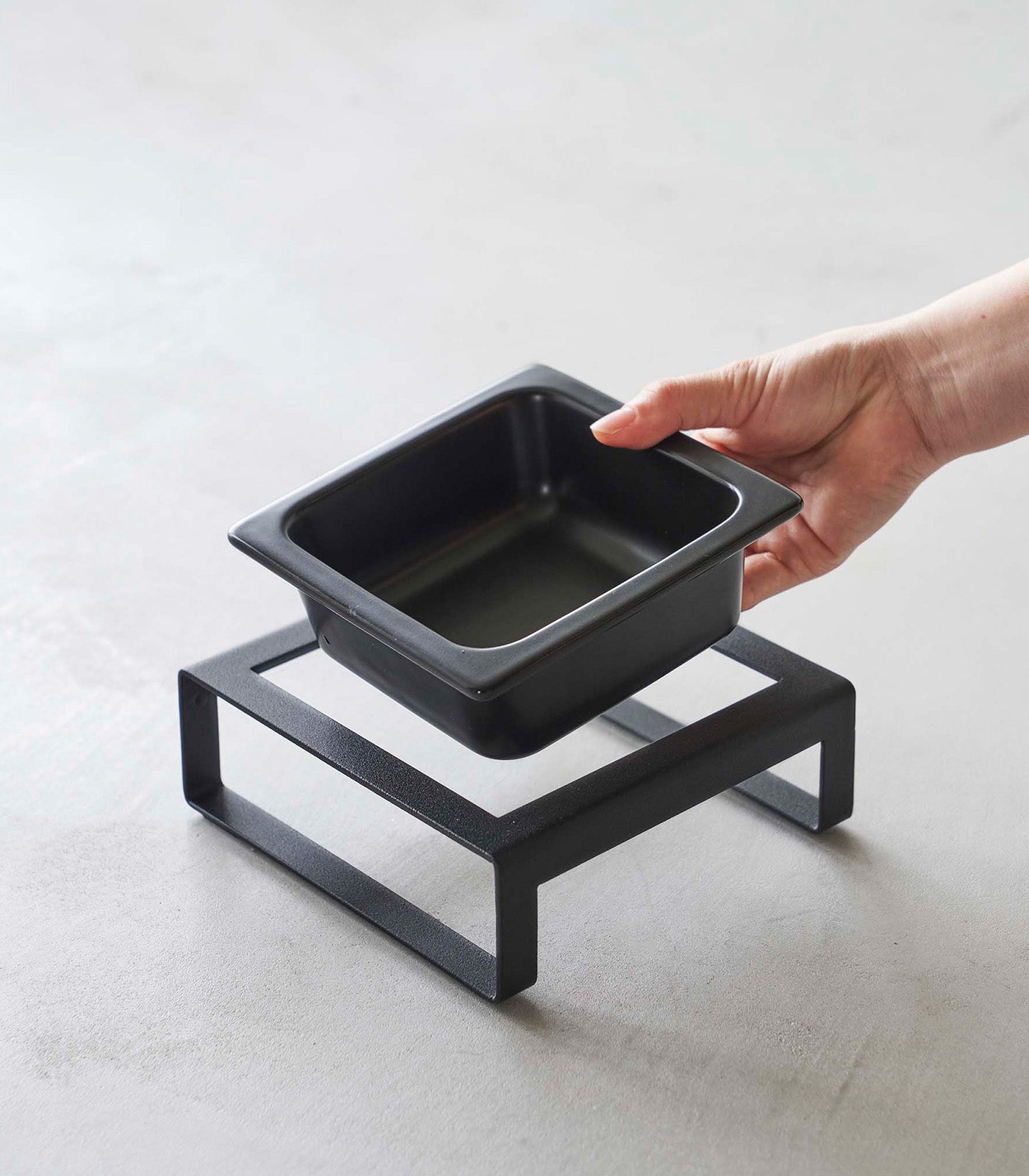 A Yamazaki Home ceramic pet food bowl on a black stand, purrfect for cats.