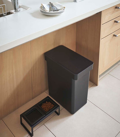 A kitchen with a black trash can on the counter and a Yamazaki Home Rolling Airtight Pet Food Container (25 Lbs.) as a kibble storage solution.