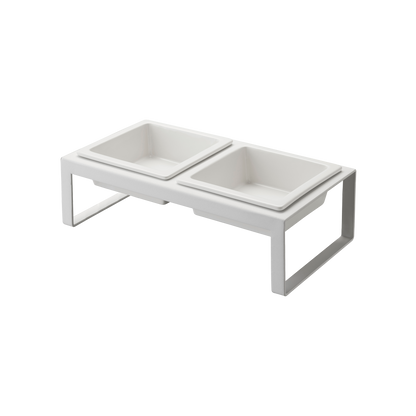 The Pet Food Bowl by Yamazaki Home is a white, elevated feeding station that includes two square ceramic bowls. Its minimalist frame provides a modern look and is designed to keep the bowls at a comfortable height for pets.