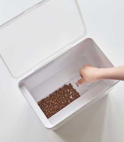 A person is using a scoop to transfer kibble into the Yamazaki Home Airtight Pet Food Container - Three Sizes.