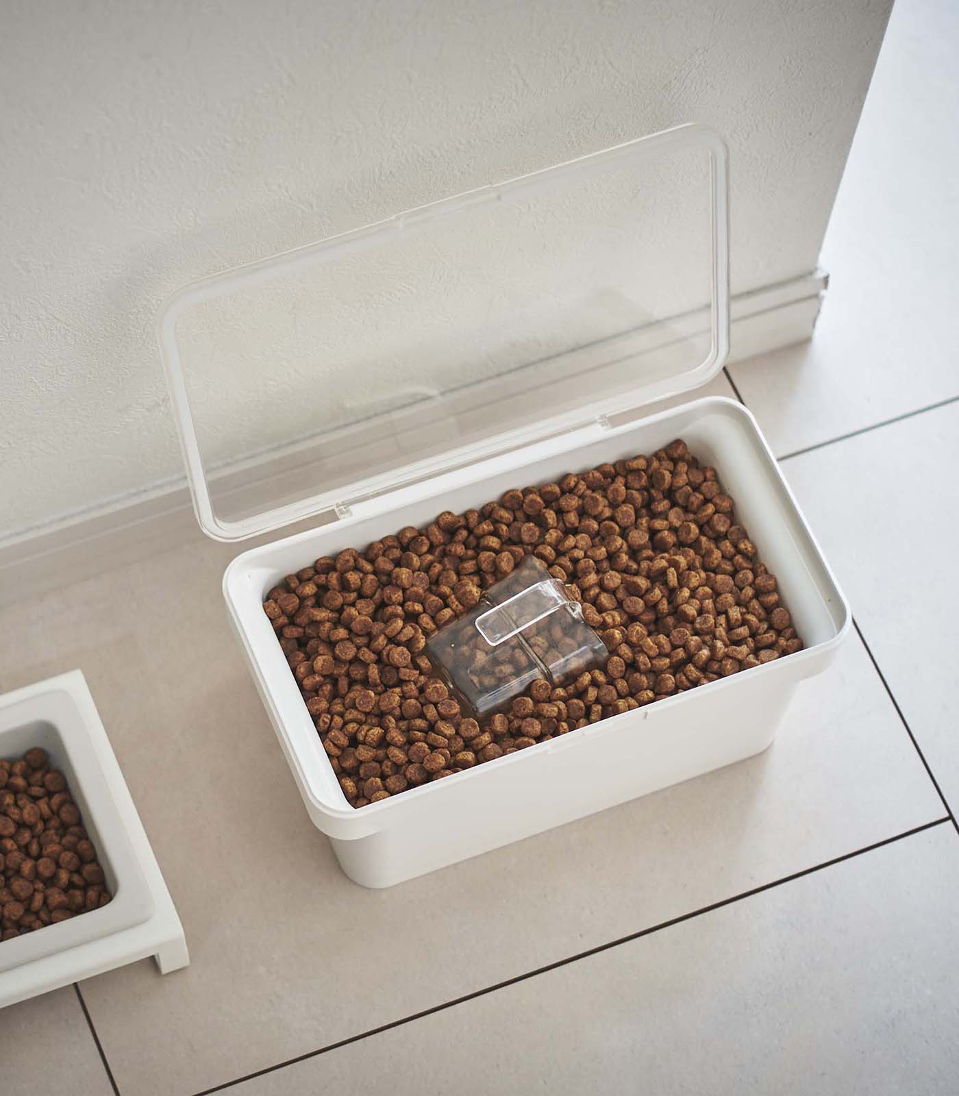 A Yamazaki Home Airtight Pet Food Container - Three Sizes, filled with kibble, placed on a tile floor.