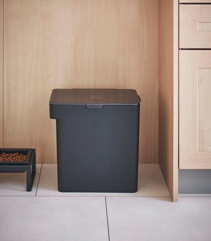 An Airtight Pet Food Container - Three Sizes by Yamazaki Home, filled with kibble, placed next to a wooden floor.