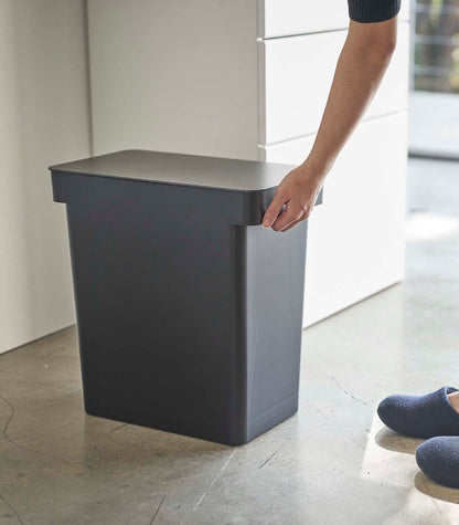 A person standing next to a black trash can with a Yamazaki Home Rolling Airtight Pet Food Container (25 Lbs.)