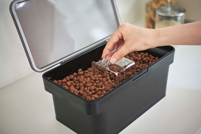 A person is using a scoop to put kibble into a Yamazaki Home Airtight Pet Food Container - Three Sizes.