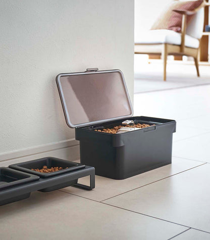 An airtight Yamazaki Home Pet Food Container - Three Sizes on the floor next to a kibble bowl.