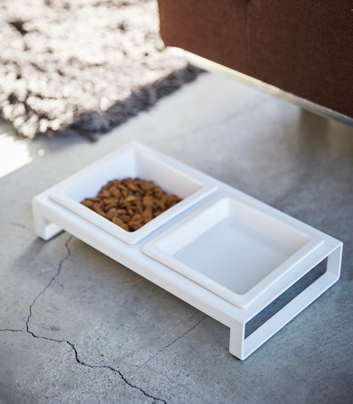 Stylish white Yamazaki Home pet feeding station with two ceramic Pet Food Bowls, one filled with kibble, on a concrete floor.
