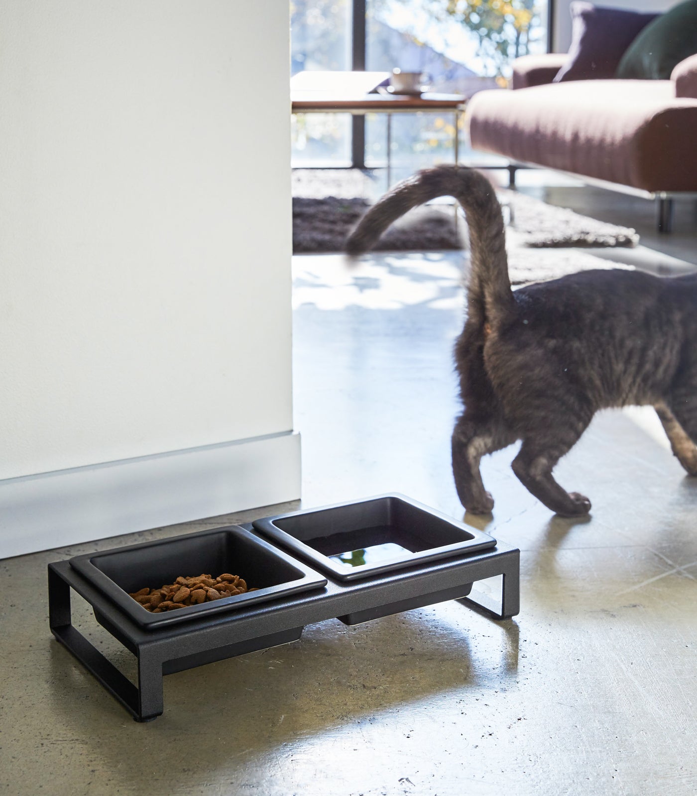 A cat walking away from a modern Yamazaki Home pet feeding station with ceramic Pet Food Bowls for food and water.
