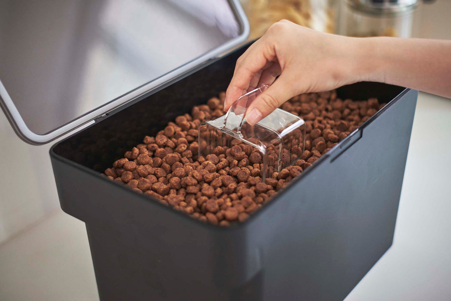 A person is using a scoop to put kibble into a Yamazaki Home Airtight Pet Food Container - Three Sizes.