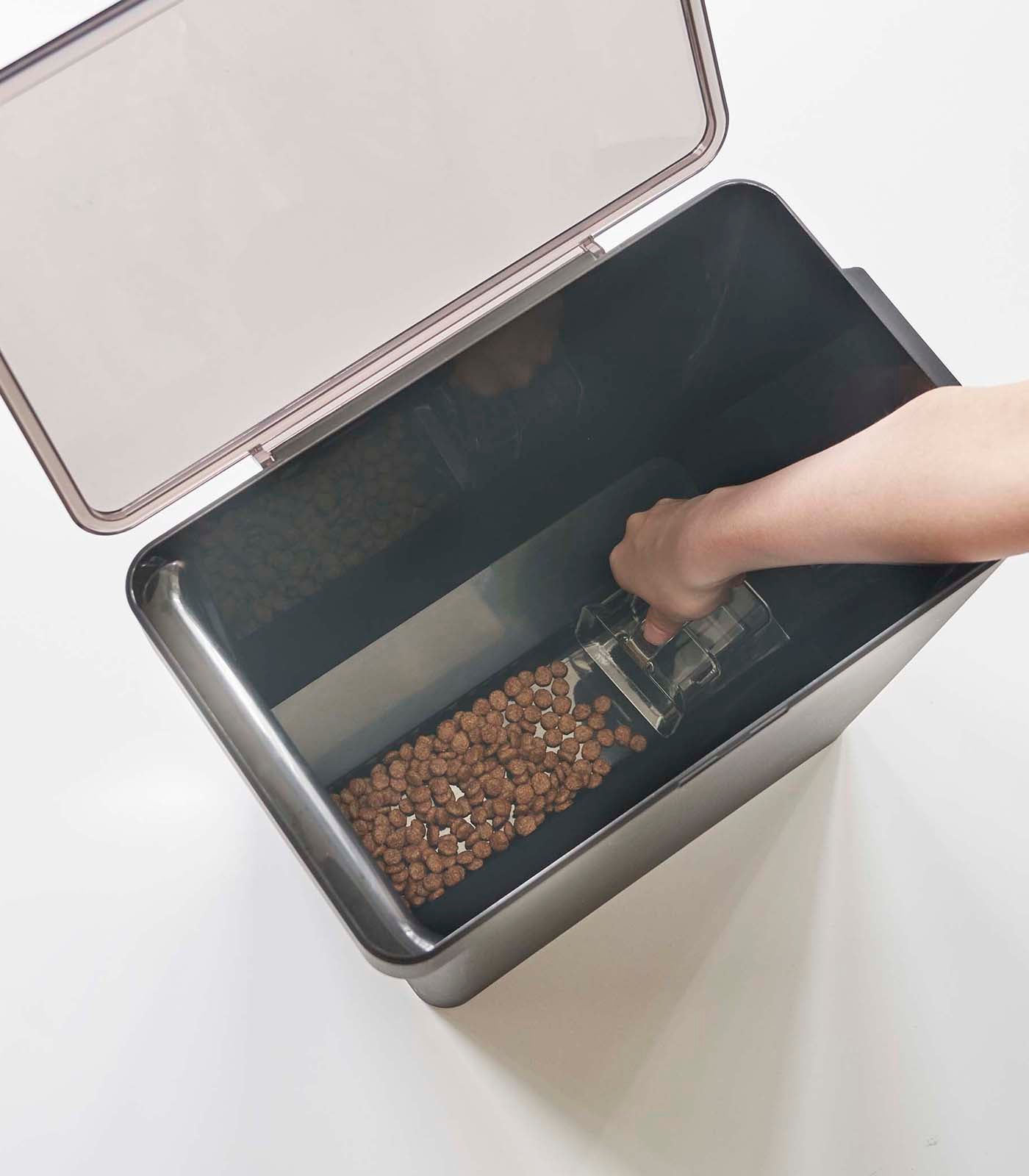 A person is using a scoop to put kibble into a Yamazaki Home Airtight Pet Food Container - Three Sizes.