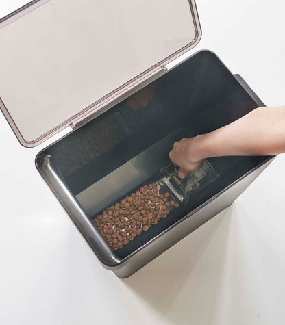 A person is using a scoop to put kibble into a Yamazaki Home Airtight Pet Food Container - Three Sizes.