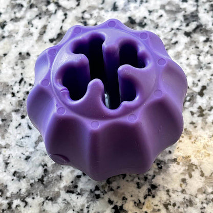 A durable Cross Bones Chew Toy and Treat Pocket from SodaPup, the purple dog toy with holes in it that dispenses treats.