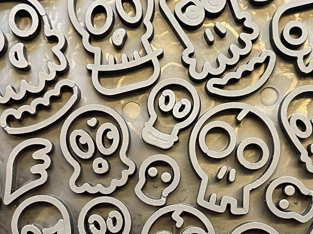 A group of Zombie Design Emat Enrichment Lick Mat skull cookie cutters on a metal plate, perfect for baking spooky treats. (Brand name: SodaPup)