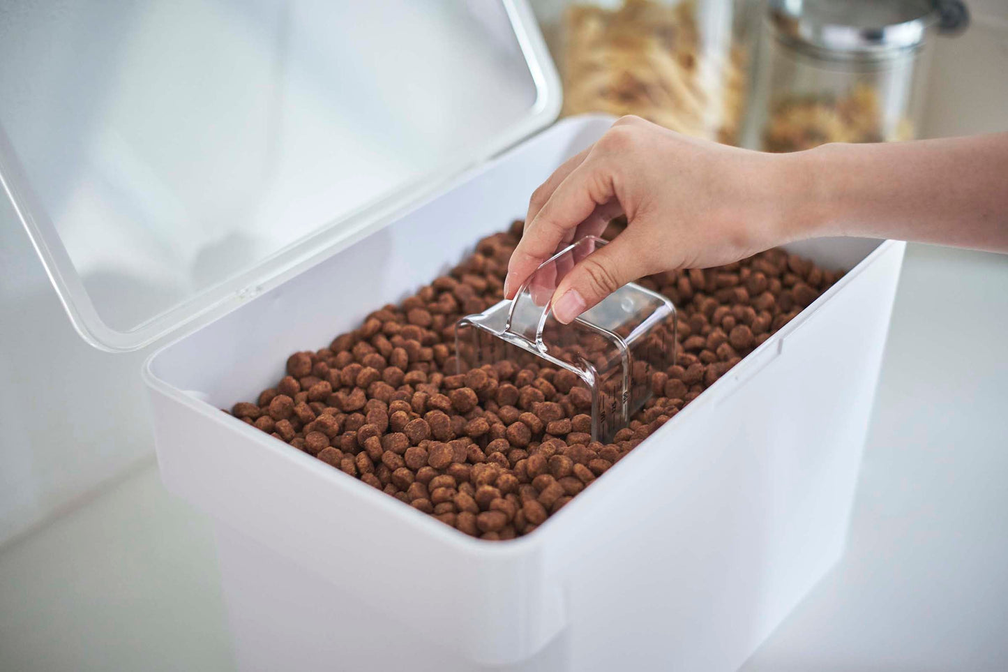 A person is scooping kibble into a Yamazaki Home Airtight Pet Food Container - Three Sizes.