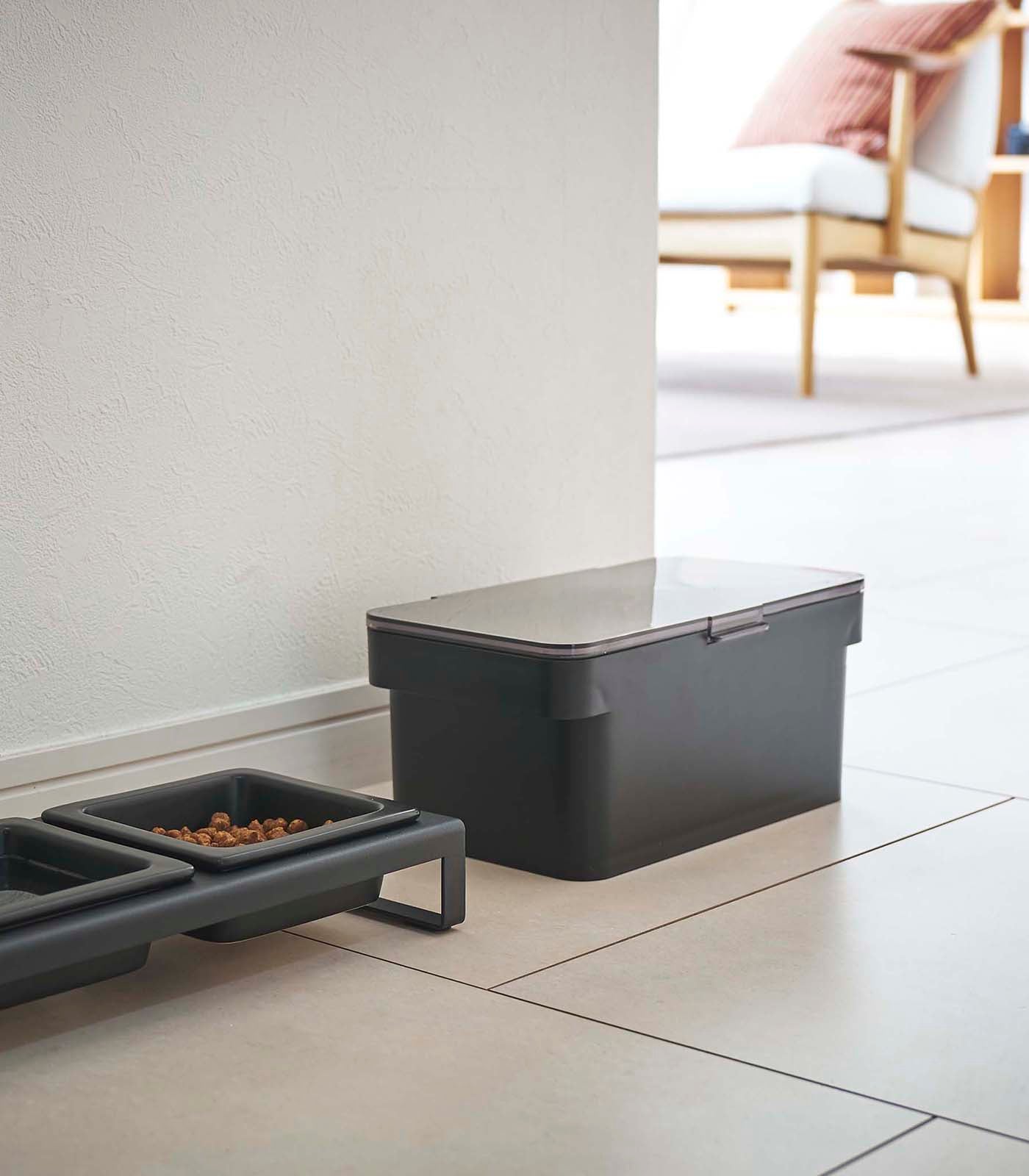 A Yamazaki Home black Airtight Pet Food Container - Three Sizes with an airtight seal on the floor next to a bowl.