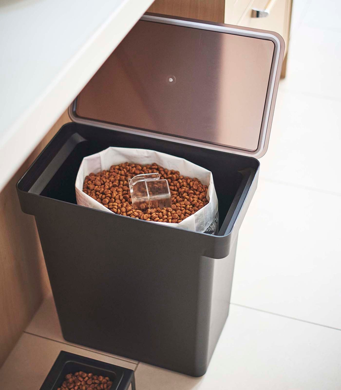 A Yamazaki Home Rolling Airtight Pet Food Container (25 Lbs.) with a lid on it next to a sink, providing an airtight kibble storage solution.