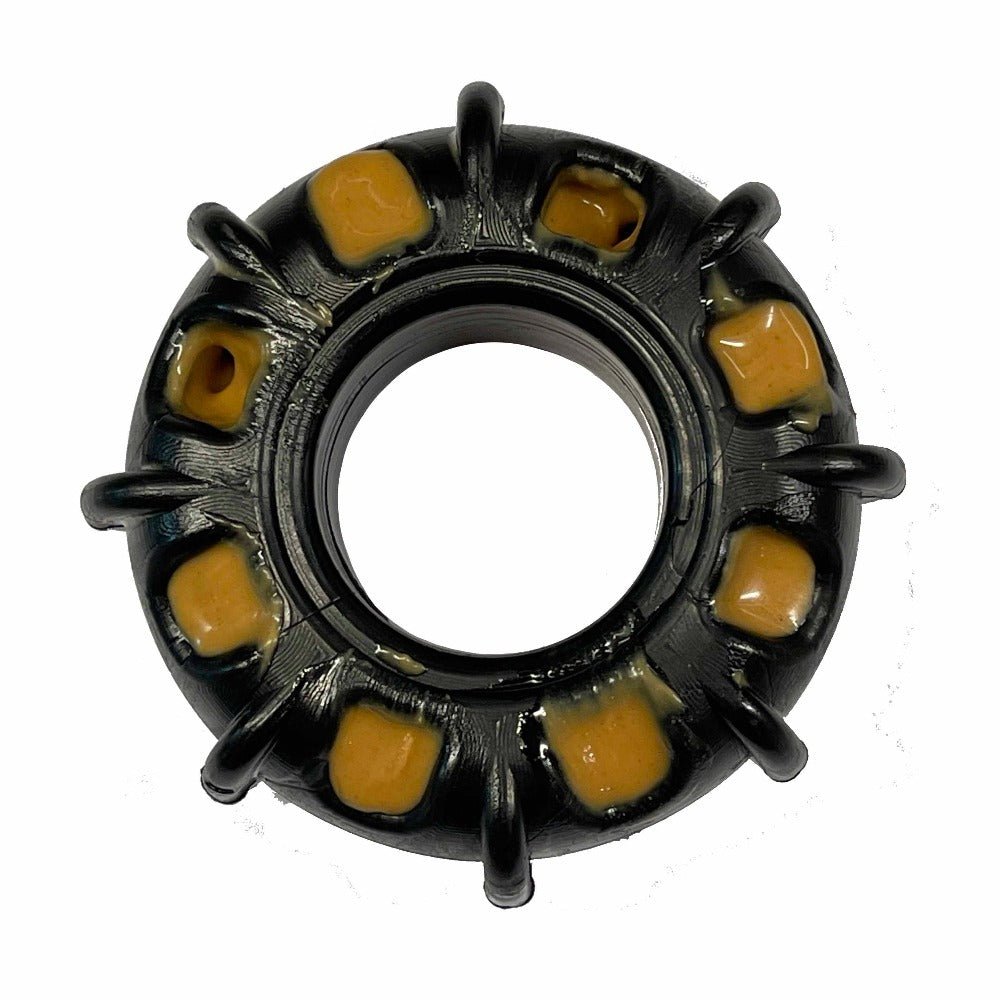 The product is a close-up of the ID Tractor Tire EChew Ultra Durable Nylon Chew & Enrichment Toy by SodaPup. It has a circular design similar to an interactive pet toy, featuring a central hole circled by eight symmetrical grooves, each with a yellowish insert. The intricate allure is enhanced by its dark and glossy material.