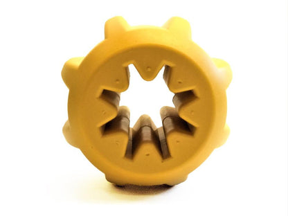 SodaPup's Gear EDispener Durable Rubber Treat Holder and Chew Toy, designed for power chewers, is a vibrant yellow. This round, gear-like rubber toy features dental ridges and a hollow center with jagged edges, perfect for inserting treats. Its vivid color and distinctive shape stand out against the white background.