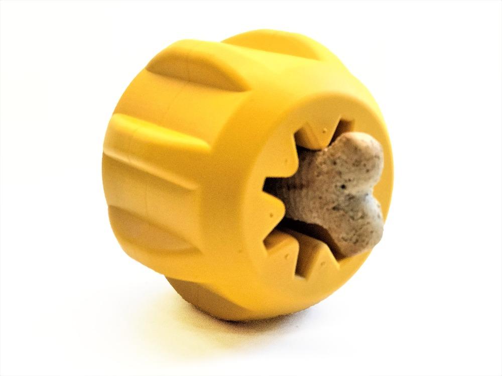 A Gear EDispener Durable Rubber Treat Holder and Chew Toy by SodaPup, in yellow with dental ridges and a tooth-like design, securely holds a brown treat at its center, making it ideal for power chewers against a white background.