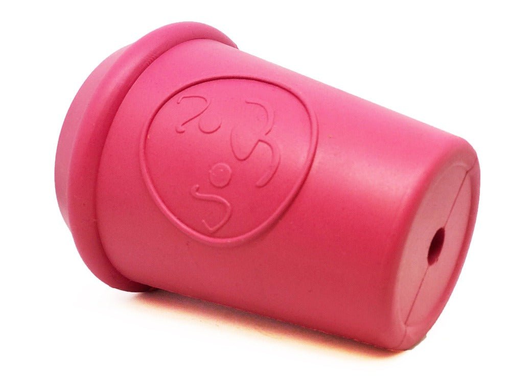 The Coffee Cup EDispener Durable Rubber Chew Toy and Treat Dispenser by SodaPup is a pink rubber dog toy shaped like a coffee cup with embossed designs. It sits upright and features a small hole at the bottom, perfect for treat dispensing or slow feeding to keep your pup entertained.