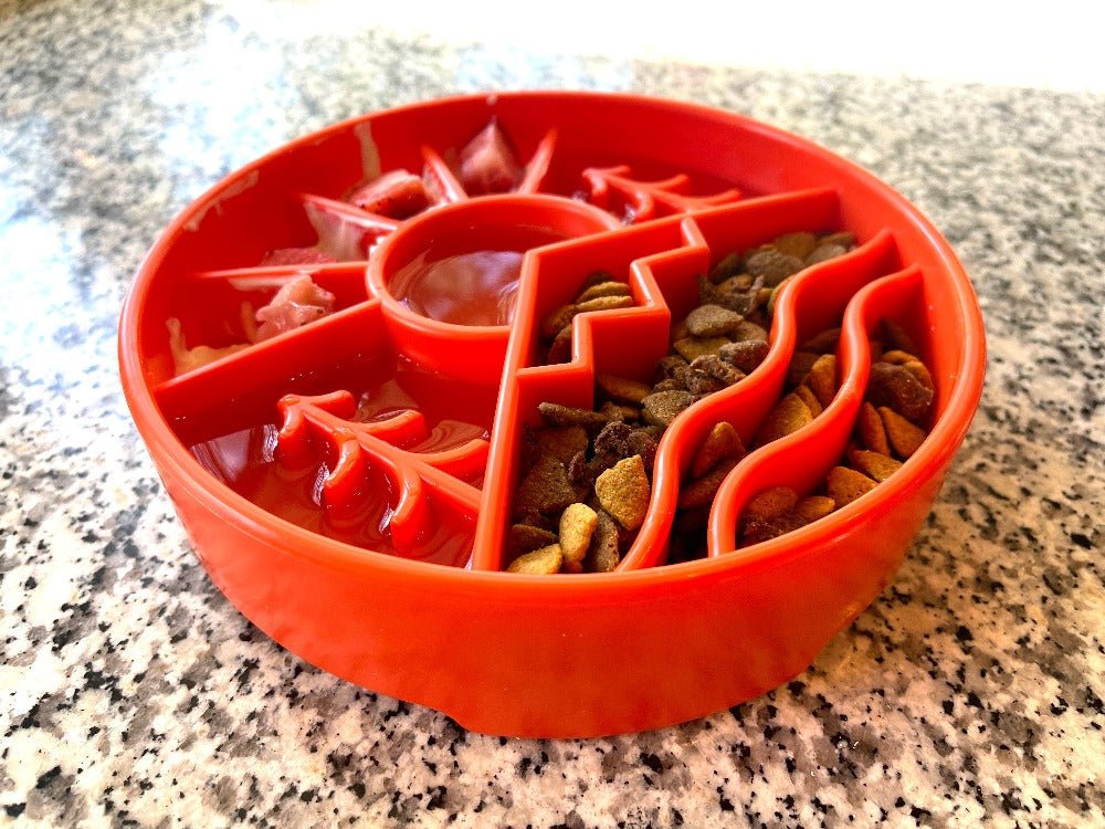 A red, round SodaPup Great Outdoors Design EBowl Enrichment Slow Feeder Bowl for Dogs, featuring multiple compartments and intricate zigzag and curved patterns to promote healthier, slower eating for your dog, filled with kibble on a speckled countertop.