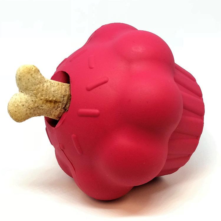 The Cupcake EDispenser Durable Rubber Chew Toy & Treat Dispenser by SodaPup is a playful red cupcake-shaped toy made from durable rubber, featuring a bone-shaped treat partially inserted in the top to cleverly dispense treats for pups.