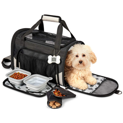 A small, fluffy beige dog sits inside an open Mobile Dog Gear Pet Carrier Plus in black, with compartments designed for a mobile dog gear feeding system, containing items like food bowls and snacks.