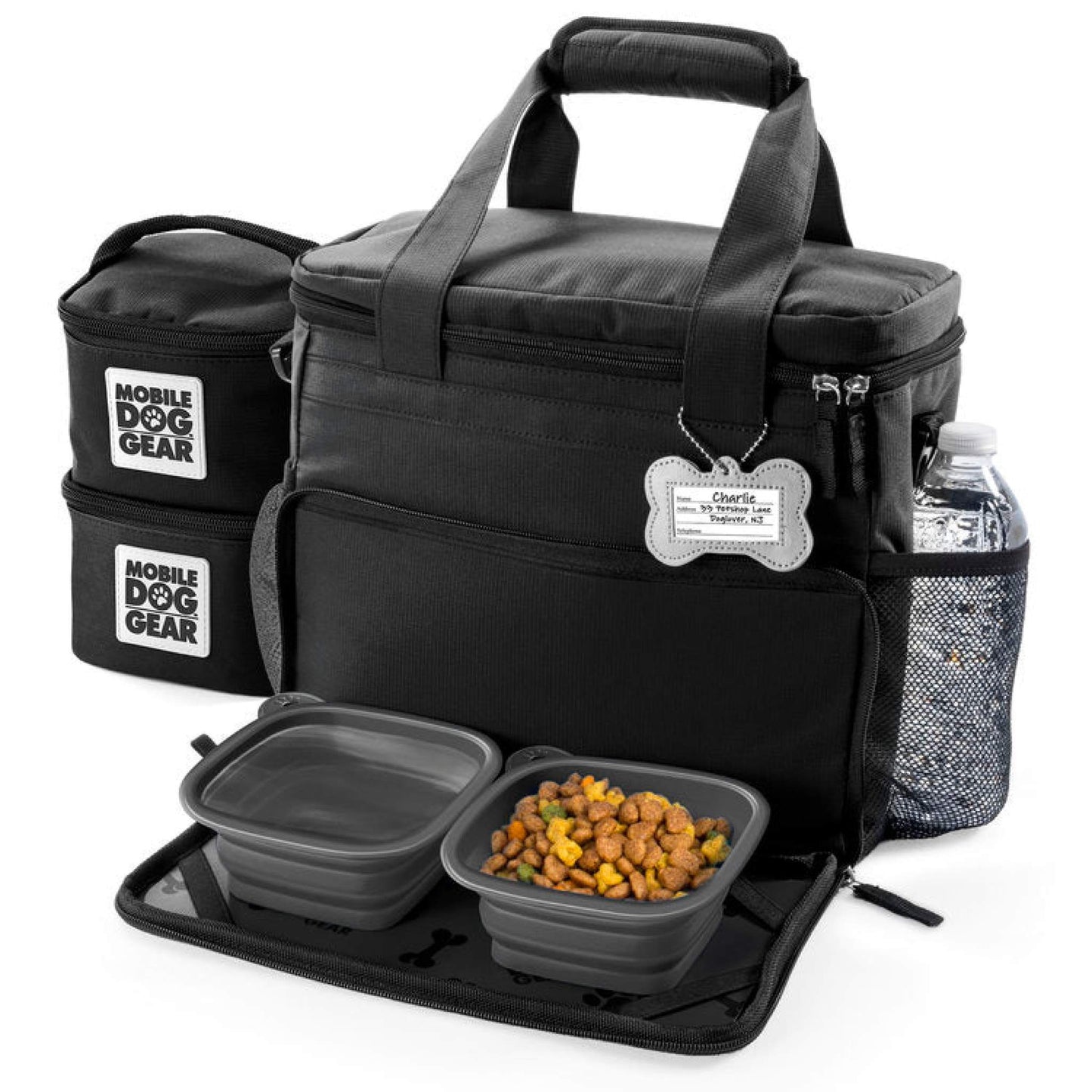 A black Mobile Dog Gear's Small Week Away® Tote Bag with accessories, including labeled side pouches, a water bottle holder, and collapsible dog bowls with dog food in an opened lower compartment.