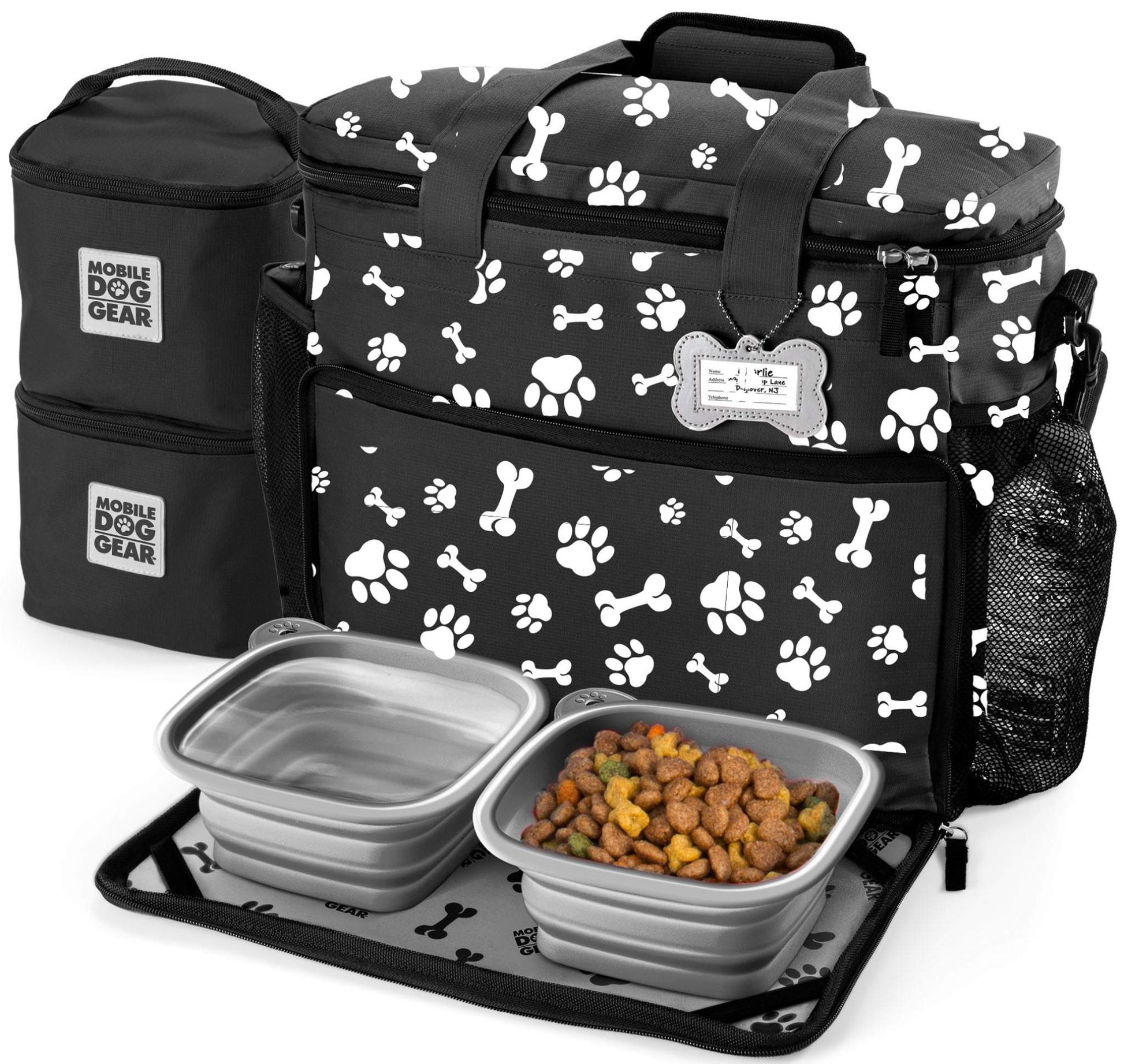 A collection of dog travel accessories including a Mobile Dog Gear Large Week Away® Tote Bag with white paw prints, two food containers with dry dog food, and a smaller insulated bag.