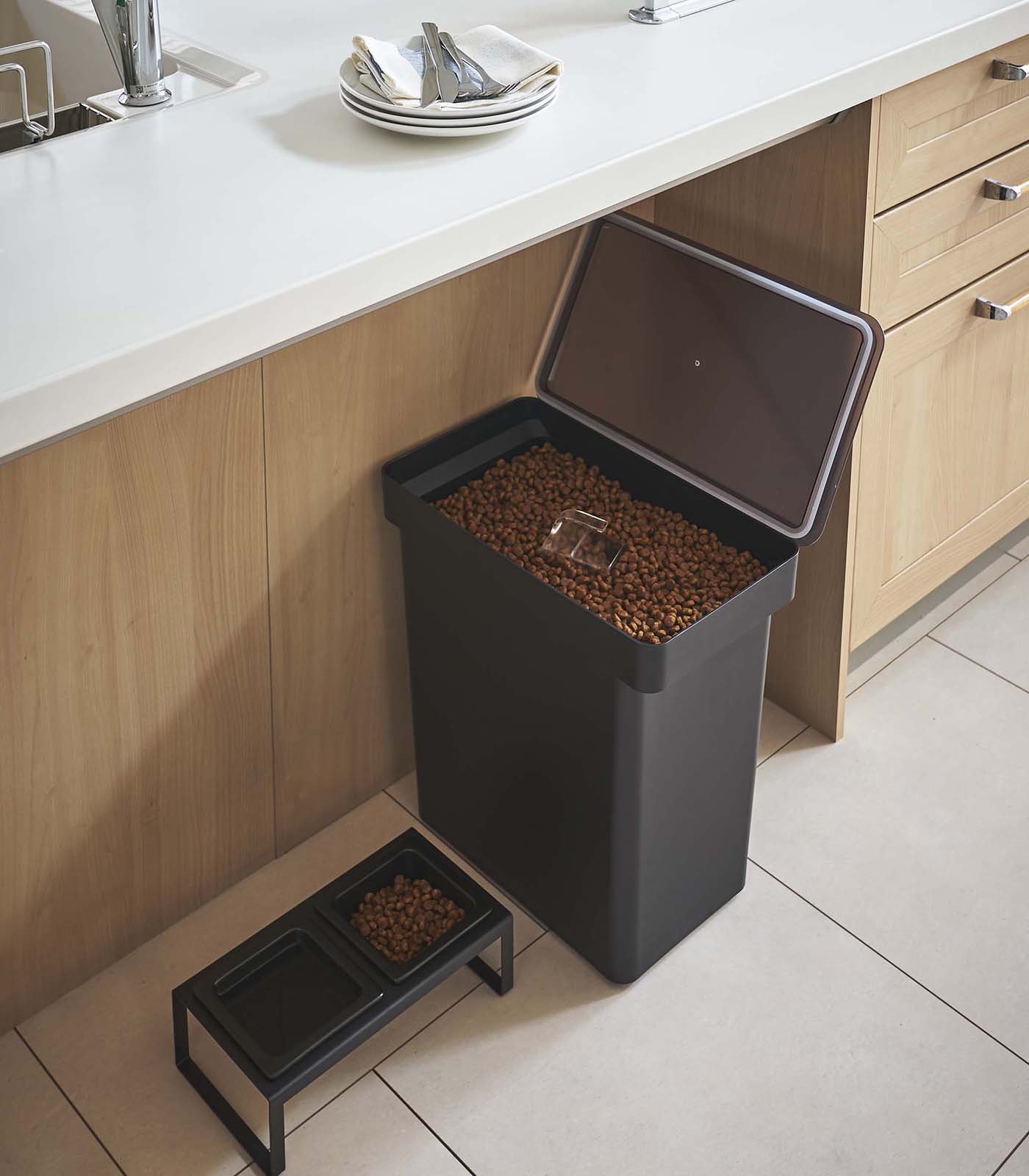 A Yamazaki Home Rolling Airtight Pet Food Container (25 Lbs.) with a lid on it next to a kitchen counter.